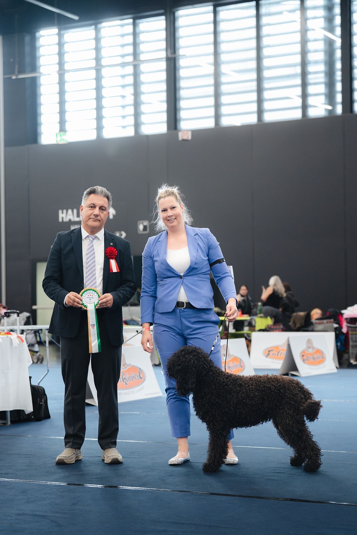 Barbet mit Hundeführerin und Richter nach der Bewertung im Ausstellungsring